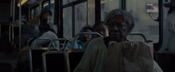 Movie still from “Samaritan” (2022), directed by Julius Avery – An older woman sitting on a bus next to a window; Medium shot, Over the shoulder angle