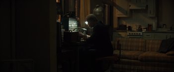 Movie still from “Samaritan” (2022), directed by Julius Avery – A man sitting at a table with a laptop; Medium shot, High angle