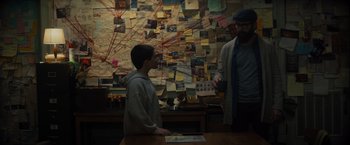 Movie still from “Samaritan” (2022), directed by Julius Avery – A boy standing in front of a wall covered in pictures; Medium shot, High angle