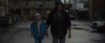 Movie still from “Samaritan” (2022), directed by Julius Avery – An older man and a young boy holding hands in front of an apartment building; Medium shot, Low angle
