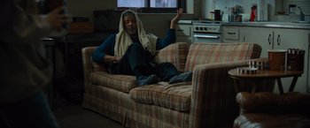 Movie still from “Samaritan” (2022), directed by Julius Avery – A man sitting on top of a couch in a living room; Medium shot, Low angle
