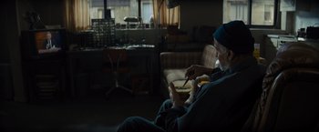 Movie still from “Samaritan” (2022), directed by Julius Avery – An older man sitting in a chair eating a bowl of food; Wide shot, High angle