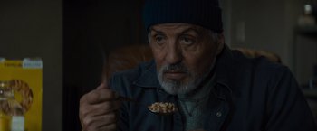 Movie still from “Samaritan” (2022), directed by Julius Avery – An older man holding a spoon with food in front of his face; Close Up shot, High angle