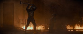 Movie still from “Samaritan” (2022), directed by Julius Avery – A baseball player holding a baseball bat in front of a fire; Wide shot, Over the shoulder angle