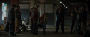 Movie still from “Samaritan” (2022), directed by Julius Avery – A man sitting on a chair in front of two other men; Wide shot, Low angle