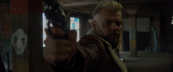 Movie still from “Samaritan” (2022), directed by Julius Avery – A person holding a gun in a room; Close Up shot, Over the shoulder angle