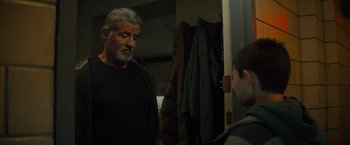 Movie still from “Samaritan” (2022), directed by Julius Avery – An older man talking to a young boy in a room; Medium shot, Over the shoulder angle