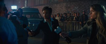 Movie still from “Samaritan” (2022), directed by Julius Avery – A woman is being interviewed by a crowd of onlookers; Medium shot, Over the shoulder angle