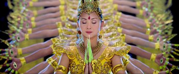 Movie still from “Samsara” (2011), directed by Ron Fricke – A woman in a yellow dress with her eyes closed and her hands in prayer position; Medium shot, Overhead angle