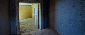 Movie still from “Samsara” (2011), directed by Ron Fricke – An open door in a room with sand on the floor; Extreme Wide shot, High angle