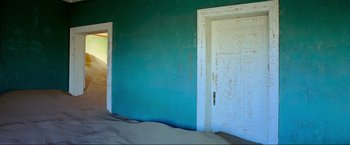 Movie still from “Samsara” (2011), directed by Ron Fricke – A room with a white door and a green wall; Extreme Wide shot, High angle