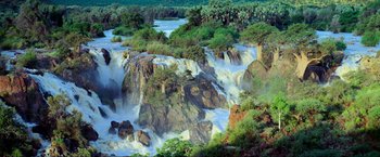 Movie still from “Samsara” (2011), directed by Ron Fricke – A large waterfall with trees in the background; Extreme Wide shot, High angle