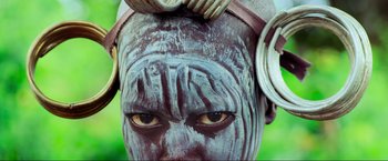 Movie still from “Samsara” (2011), directed by Ron Fricke – A person with a painted face and horns on their head; Extreme Close Up shot, Overhead angle