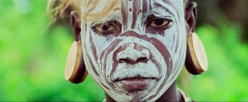 Movie still from “Samsara” (2011), directed by Ron Fricke – A person with a painted face is looking into the camera; Extreme Close Up shot, High angle