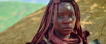 Movie still from “Samsara” (2011), directed by Ron Fricke – A woman with long dreadlocks is standing in the sand; Close Up shot, Over the shoulder angle