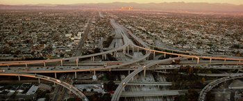 Movie still from “Samsara” (2011), directed by Ron Fricke – An aerial view of a freeway with a city in the background; Extreme Wide shot, Overhead angle