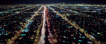 Movie still from “Samsara” (2011), directed by Ron Fricke – An aerial view of a city at night with cars driving down the road; Extreme Wide shot, Overhead angle