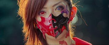 Movie still from “Samsara” (2011), directed by Ron Fricke – A woman with red , black , and purple makeup on her face; Extreme Close Up shot, High angle