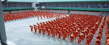 Movie still from “Samsara” (2011), directed by Ron Fricke – A large group of people in orange jumpsuits; Extreme Wide shot, High angle