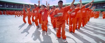 Movie still from “Samsara” (2011), directed by Ron Fricke – A group of young men in orange jumpsuits are dancing; Wide shot, Overhead angle