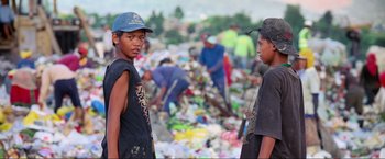Movie still from “Samsara” (2011), directed by Ron Fricke – Two young men standing next to a pile of garbage; Medium shot, High angle