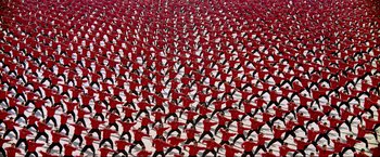 Movie still from “Samsara” (2011), directed by Ron Fricke – A large group of men in red shirts doing different exercises; Extreme Wide shot, Overhead angle