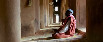 Movie still from “Samsara” (2011), directed by Ron Fricke – A man sitting on the floor of a building; Wide shot, High angle