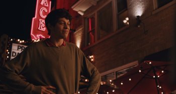 Movie still from “Big Time Adolescence” (2019), directed by Jason Orley – A man standing in front of a building with lights in the background; Medium shot, Over the shoulder angle