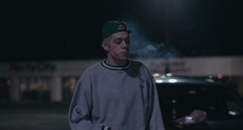 Movie still from “Big Time Adolescence” (2019), directed by Jason Orley – A man in a green hat is smoking a cigarette; Medium shot, Over the shoulder angle