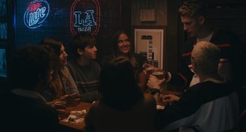 Movie still from “Big Time Adolescence” (2019), directed by Jason Orley – A group of people sitting at a table with drinks; Medium shot, Over the shoulder angle