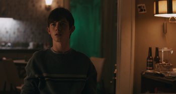 Movie still from “Big Time Adolescence” (2019), directed by Jason Orley – A young man is sitting in front of a green light; Medium shot, Over the shoulder angle