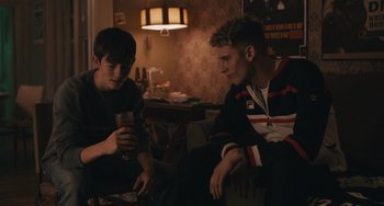 Movie still from “Big Time Adolescence” (2019), directed by Jason Orley – Two young men sitting in a living room drinking wine; Medium shot, Over the shoulder angle