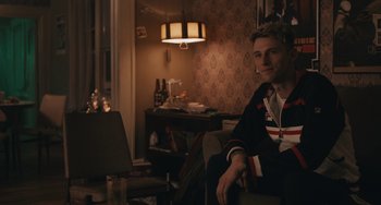 Movie still from “Big Time Adolescence” (2019), directed by Jason Orley – A man sitting on a chair in a living room; Medium shot, Over the shoulder angle