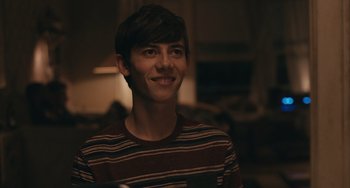 Movie still from “Big Time Adolescence” (2019), directed by Jason Orley – A young man smiling for the camera in the dark; Close Up shot, Over the shoulder angle