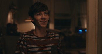 Movie still from “Big Time Adolescence” (2019), directed by Jason Orley – A young man in a striped shirt is smiling; Close Up shot, Over the shoulder angle
