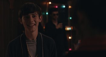 Movie still from “Big Time Adolescence” (2019), directed by Jason Orley – A young man smiling at the camera in front of some lights; Close Up shot, Over the shoulder angle