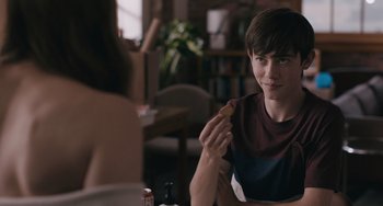 Movie still from “Big Time Adolescence” (2019), directed by Jason Orley – A young man sitting at a table eating a cookie; Close Up shot, Over the shoulder angle