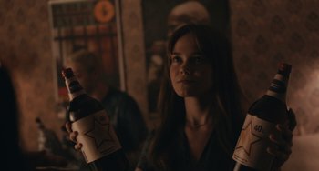 Movie still from “Big Time Adolescence” (2019), directed by Jason Orley – A woman holding a bottle of wine in a dark room; Close Up shot, Over the shoulder angle