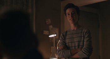Movie still from “Big Time Adolescence” (2019), directed by Jason Orley – A young man standing with his arms crossed in front of a lamp; Medium shot, Over the shoulder angle