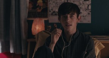 Movie still from “Big Time Adolescence” (2019), directed by Jason Orley – A young man is listening to music while holding his ear buds; Close Up shot, Over the shoulder angle