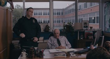 Movie still from “Big Time Adolescence” (2019), directed by Jason Orley – A man sitting at a desk in front of another man; Medium shot, Over the shoulder angle