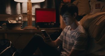 Movie still from “Big Time Adolescence” (2019), directed by Jason Orley – A man sitting on the ground looking at a phone; Medium shot, High angle