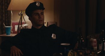 Movie still from “Big Time Adolescence” (2019), directed by Jason Orley – A man in a police uniform standing next to a table; Medium shot, Over the shoulder angle