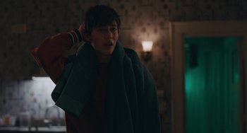Movie still from “Big Time Adolescence” (2019), directed by Jason Orley – A young man wrapped in a blanket in a dark room; Medium shot, Over the shoulder angle