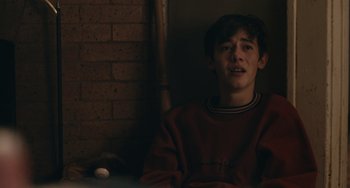 Movie still from “Big Time Adolescence” (2019), directed by Jason Orley – A young man sitting in front of a brick wall; Medium shot, Over the shoulder angle