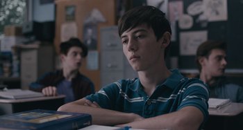 Movie still from “Big Time Adolescence” (2019), directed by Jason Orley – A boy sitting at a table with his arms crossed; Close Up shot, Over the shoulder angle
