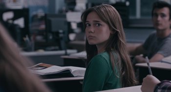 Movie still from “Big Time Adolescence” (2019), directed by Jason Orley – A girl sitting at a desk in an office setting; Close Up shot, Over the shoulder angle