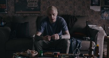 Movie still from “Big Time Adolescence” (2019), directed by Jason Orley – A man sitting on a couch holding a cigarette; Medium shot, Low angle