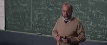 Movie still from “San Andreas” (2015), directed by Brad Peyton – A man standing in front of a chalkboard holding a cell phone; Medium shot, Over the shoulder angle