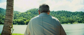 Movie still from “Savage Salvation” (2022), directed by Randall Emmett – An older man wearing a tan shirt looking out over a forest; Medium shot, Over the shoulder angle